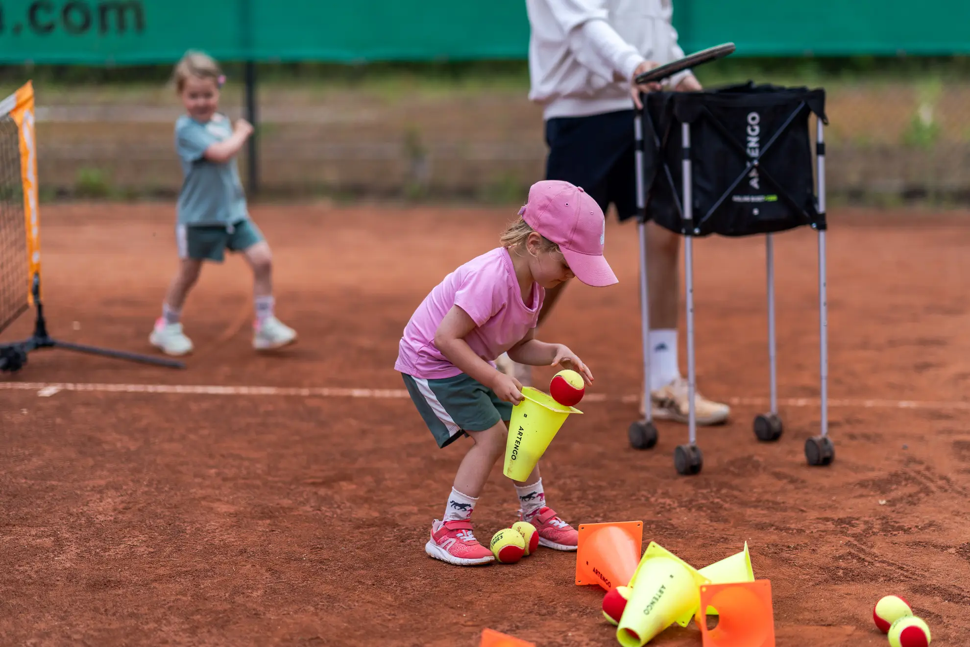 Mädchen sammelt Tennisbälle in einem Hütchen.