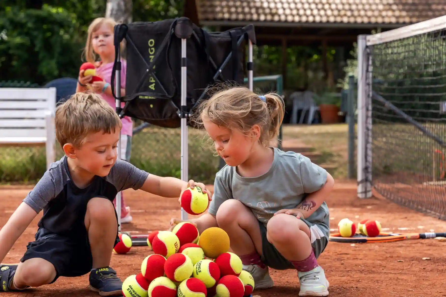Mädchen und Junge bauen eine Pyramide aus Tennisbällen.